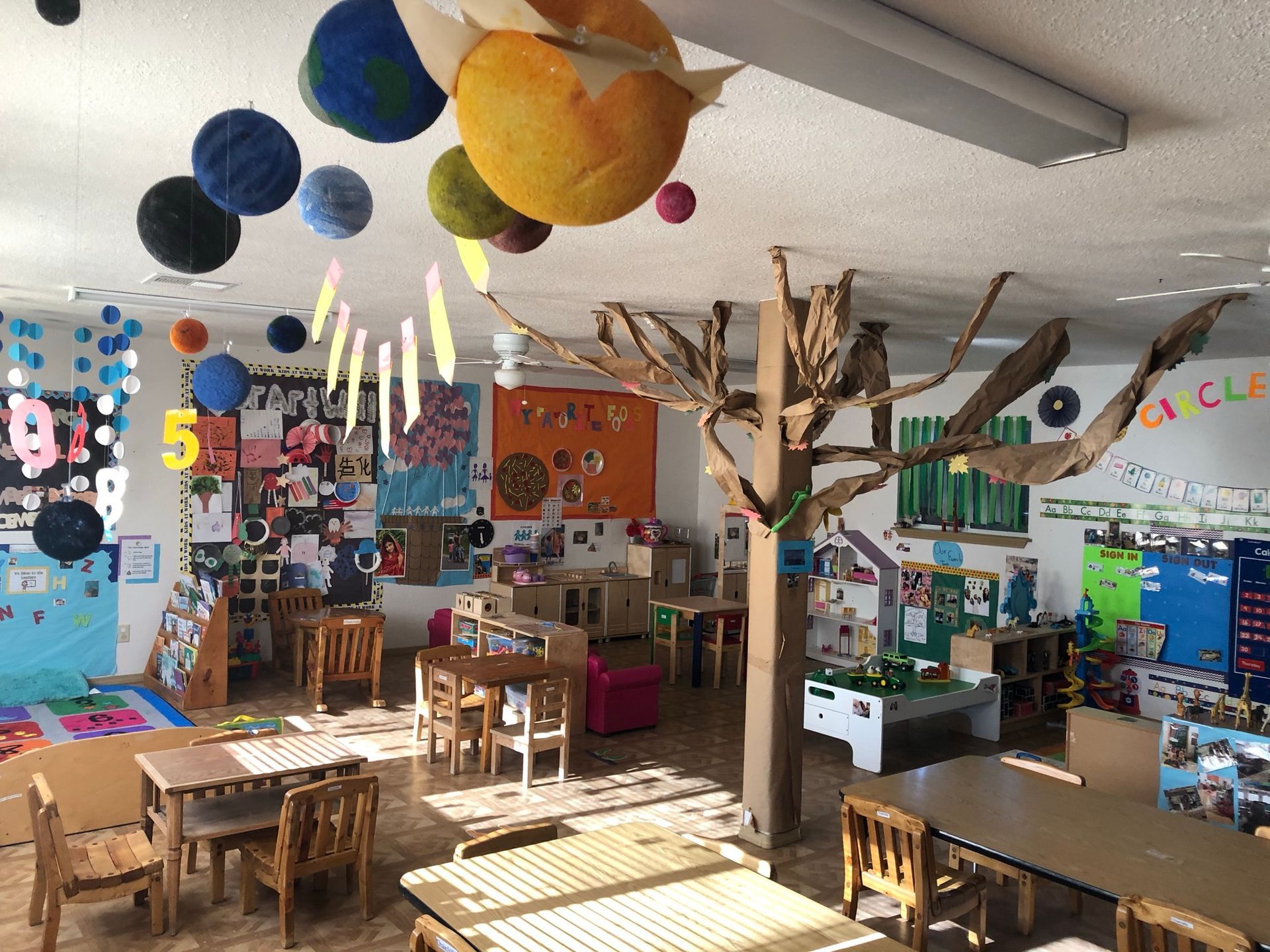A classroom with tables and chairs and a tree hanging from the ceiling.
