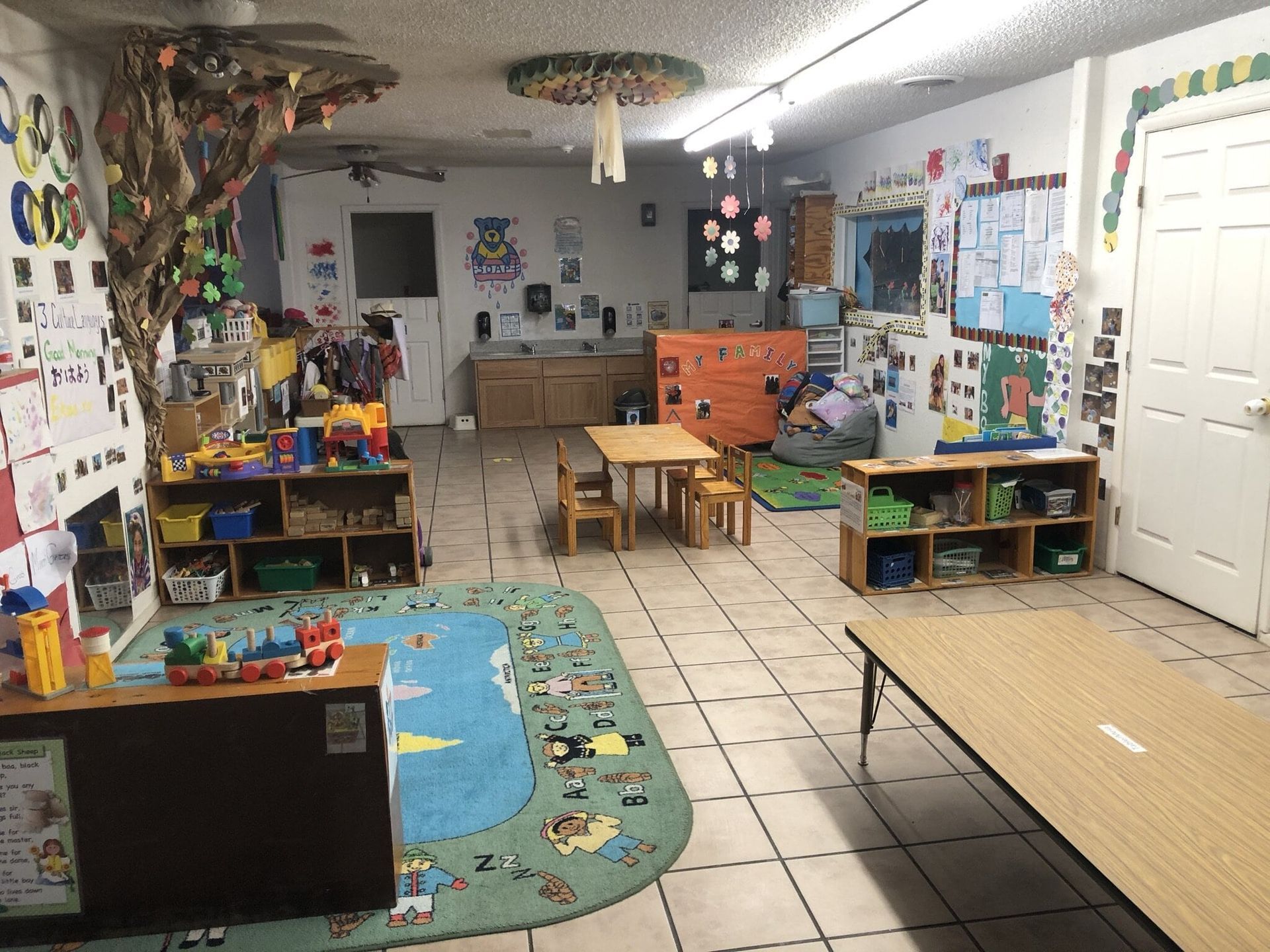 A classroom with tables and chairs and a rug on the floor.