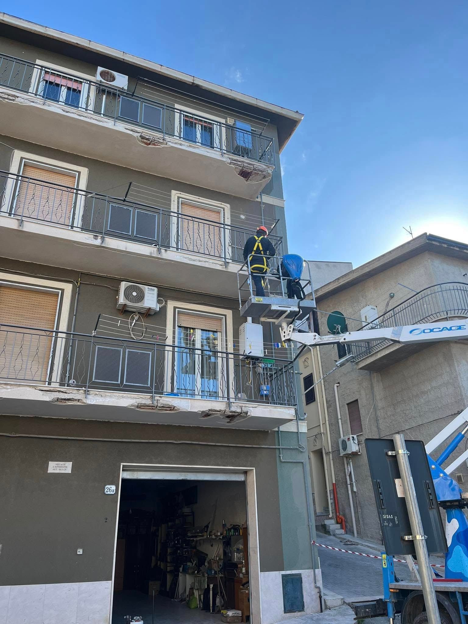 Vigili del fuoco su un ascensore al lavoro su un edificio. Edificio grigio con balconi, cielo azzurro.