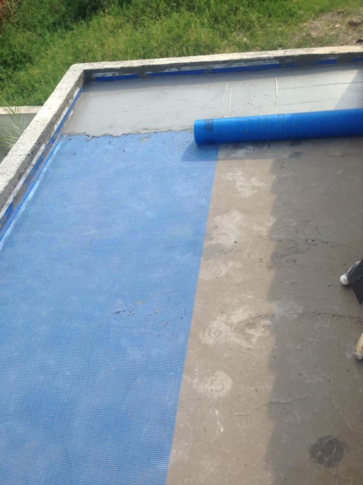 Materiale a rete blu che ricopre parzialmente una superficie di cemento grigio, con una sezione arrotolata visibile.