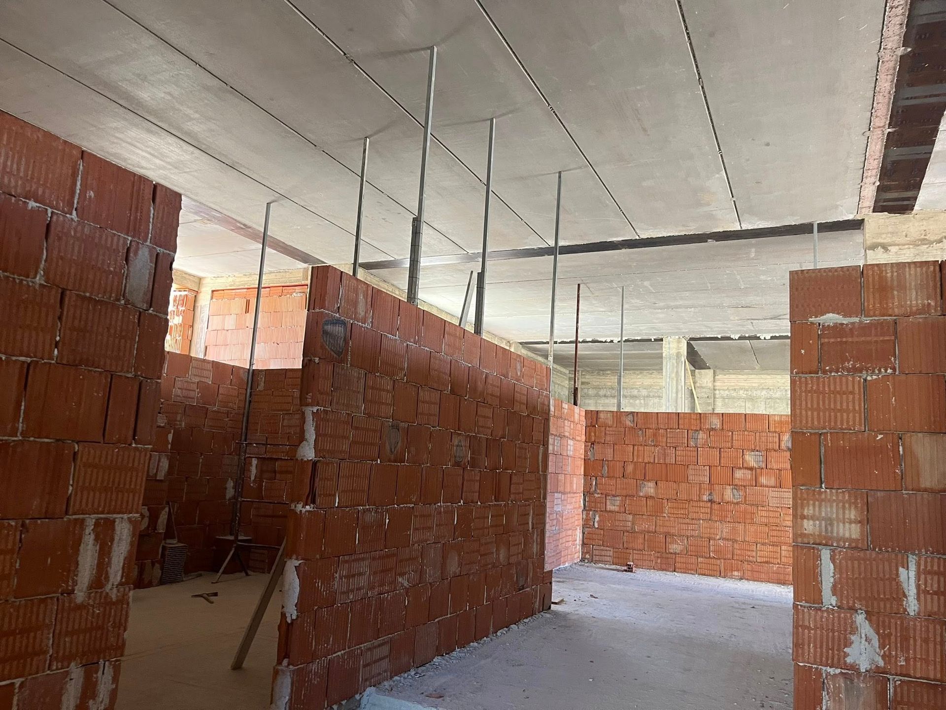 Interno di un edificio in costruzione. Pareti in mattoni rossi, soffitto in cemento, supporti metallici.