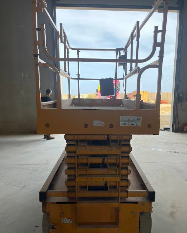 Piattaforma elevatrice a forbice gialla all'interno di un edificio con una persona in piedi dietro, che guarda verso l'esterno.