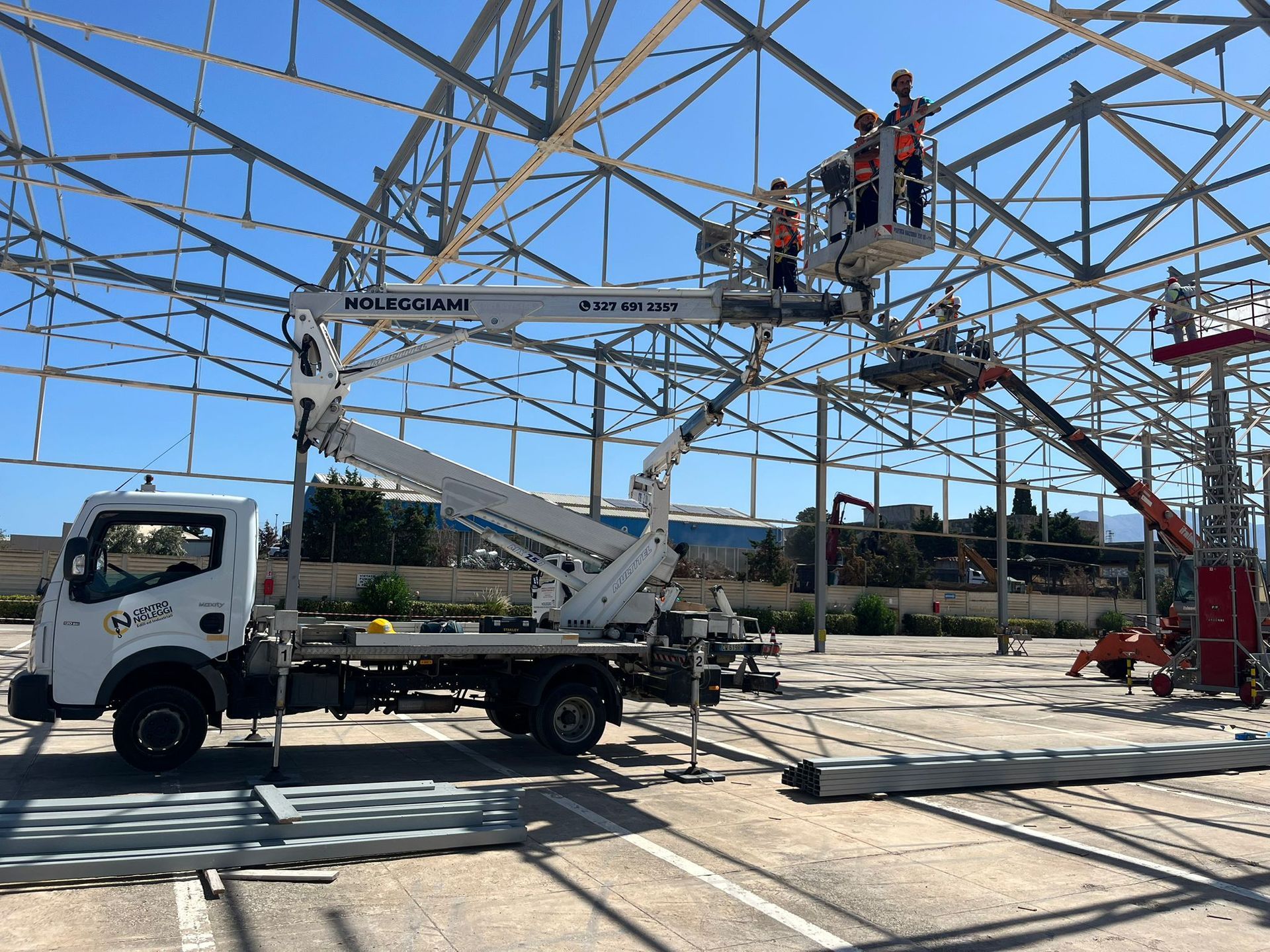 Due piattaforme aeree montate su camion, con piattaforme estese in alto contro un cielo azzurro, di fronte a un edificio.