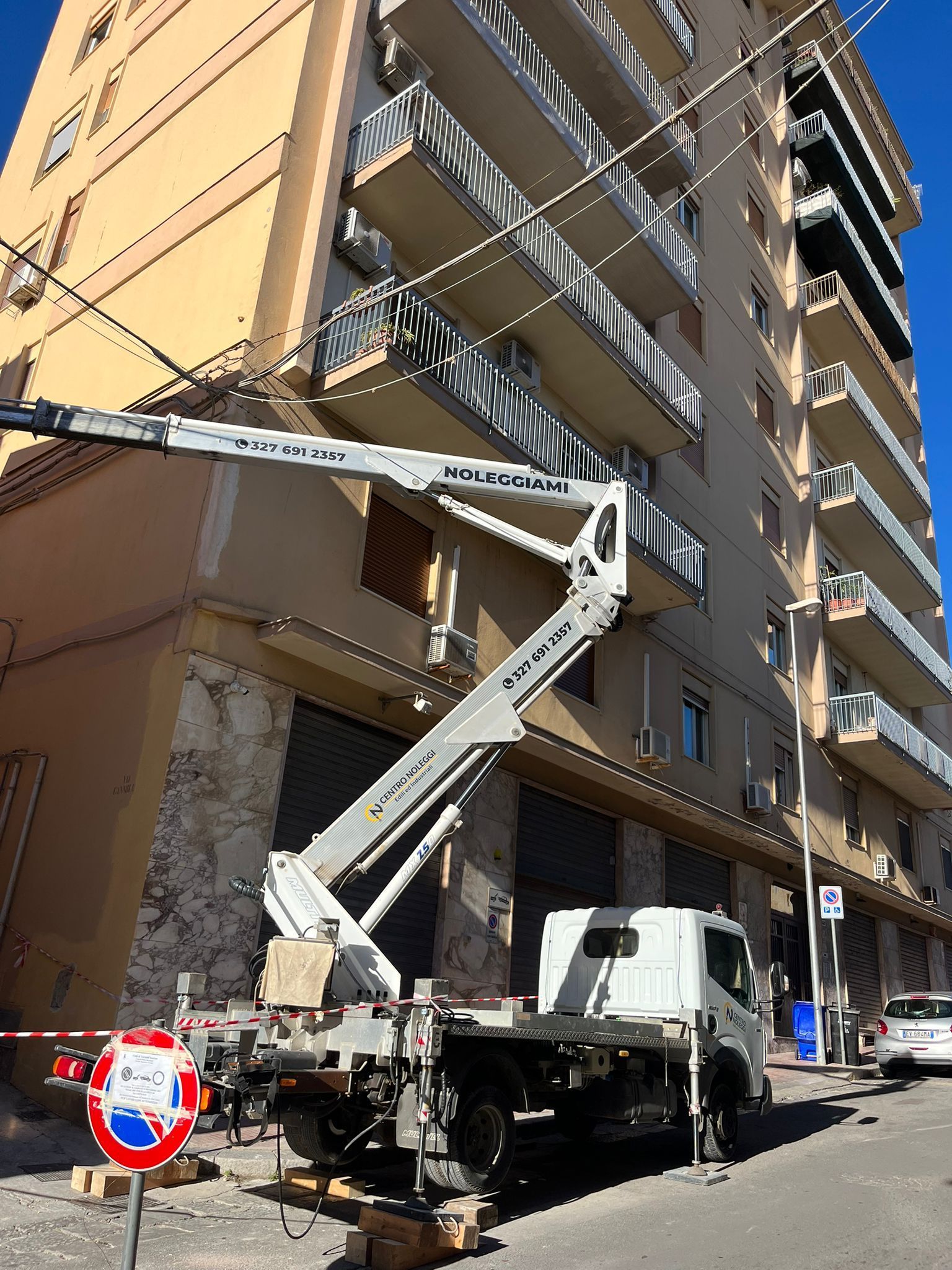 Un veicolo Manitou rosso e una gru gialla parcheggiati vicino a un edificio in una giornata di sole.