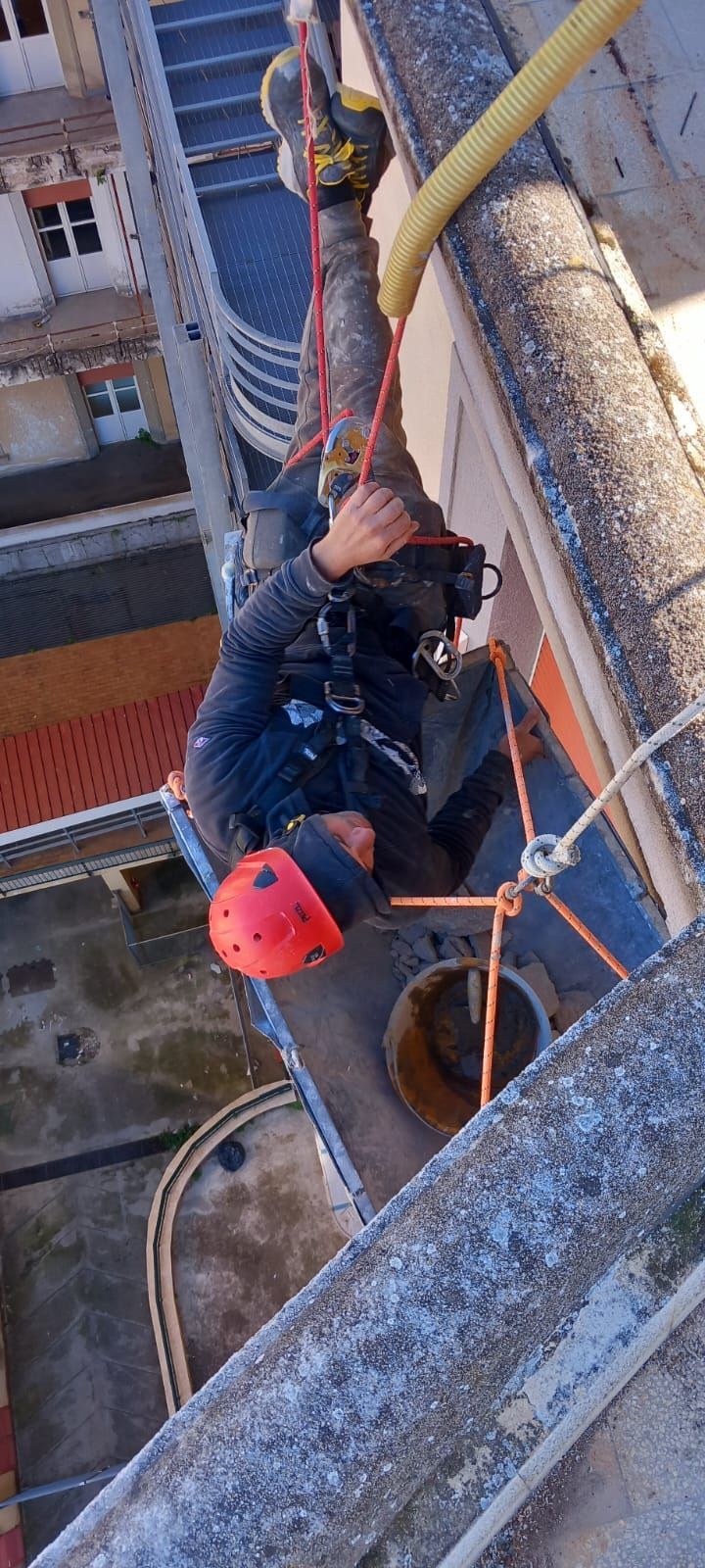 Camion con sollevatore accanto a un edificio giallo. Operai nelle vicinanze. Cielo azzurro brillante.