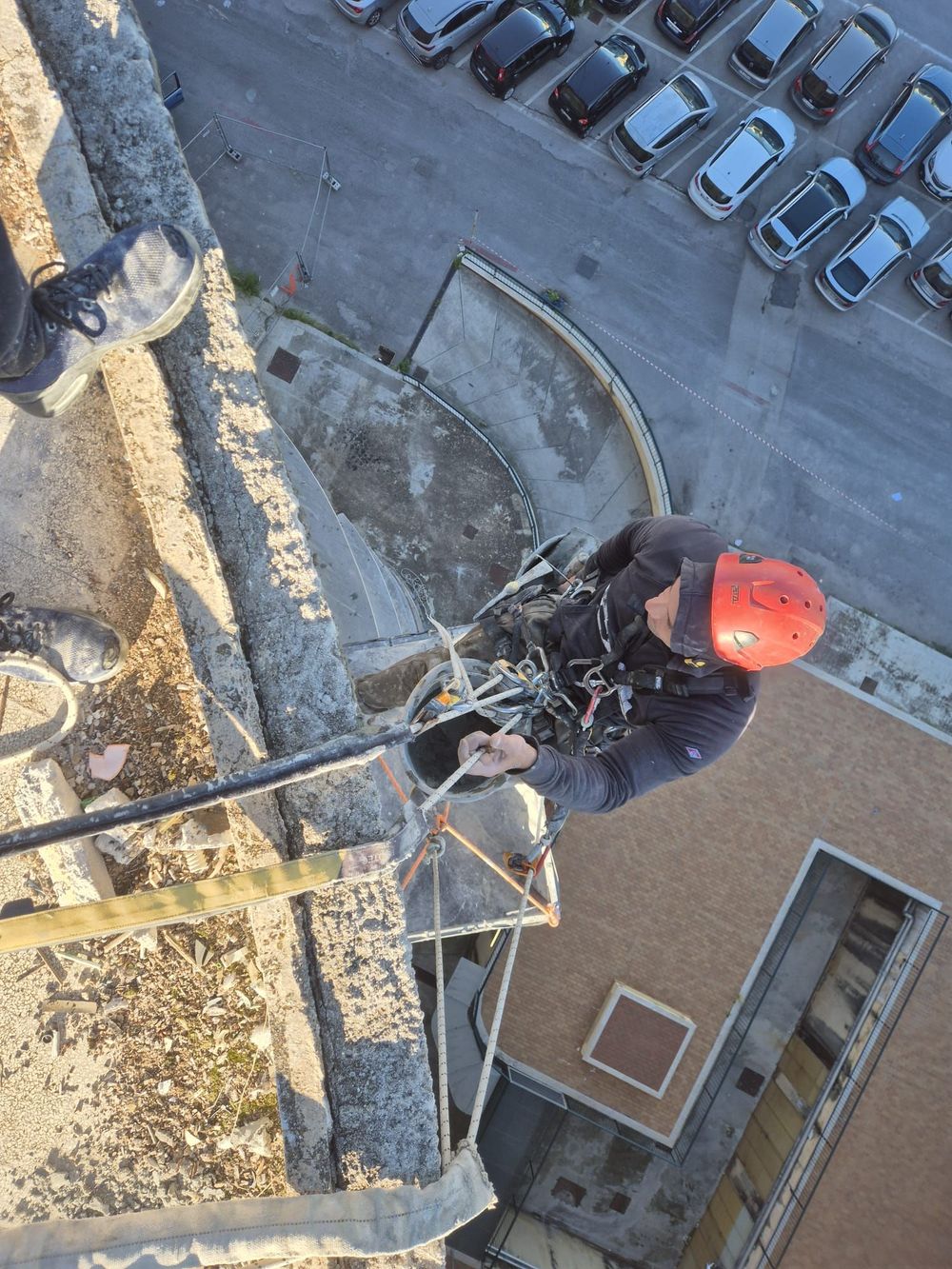 Un operaio si cala in corda doppia da un edificio, indossando imbracatura e casco, mentre ispeziona un balcone.