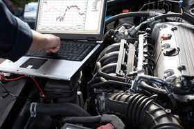 a man is working on a car engine while using a laptop for diagnostic