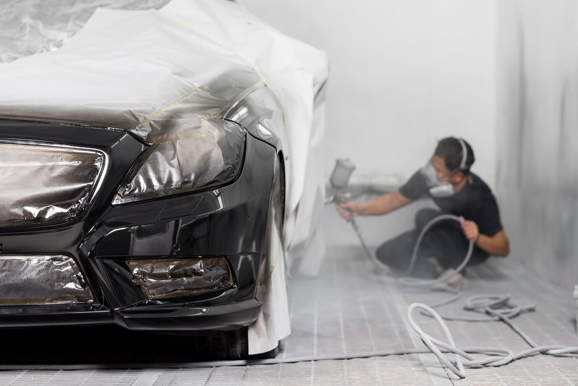 a man is spray painting a black car in a paint booth