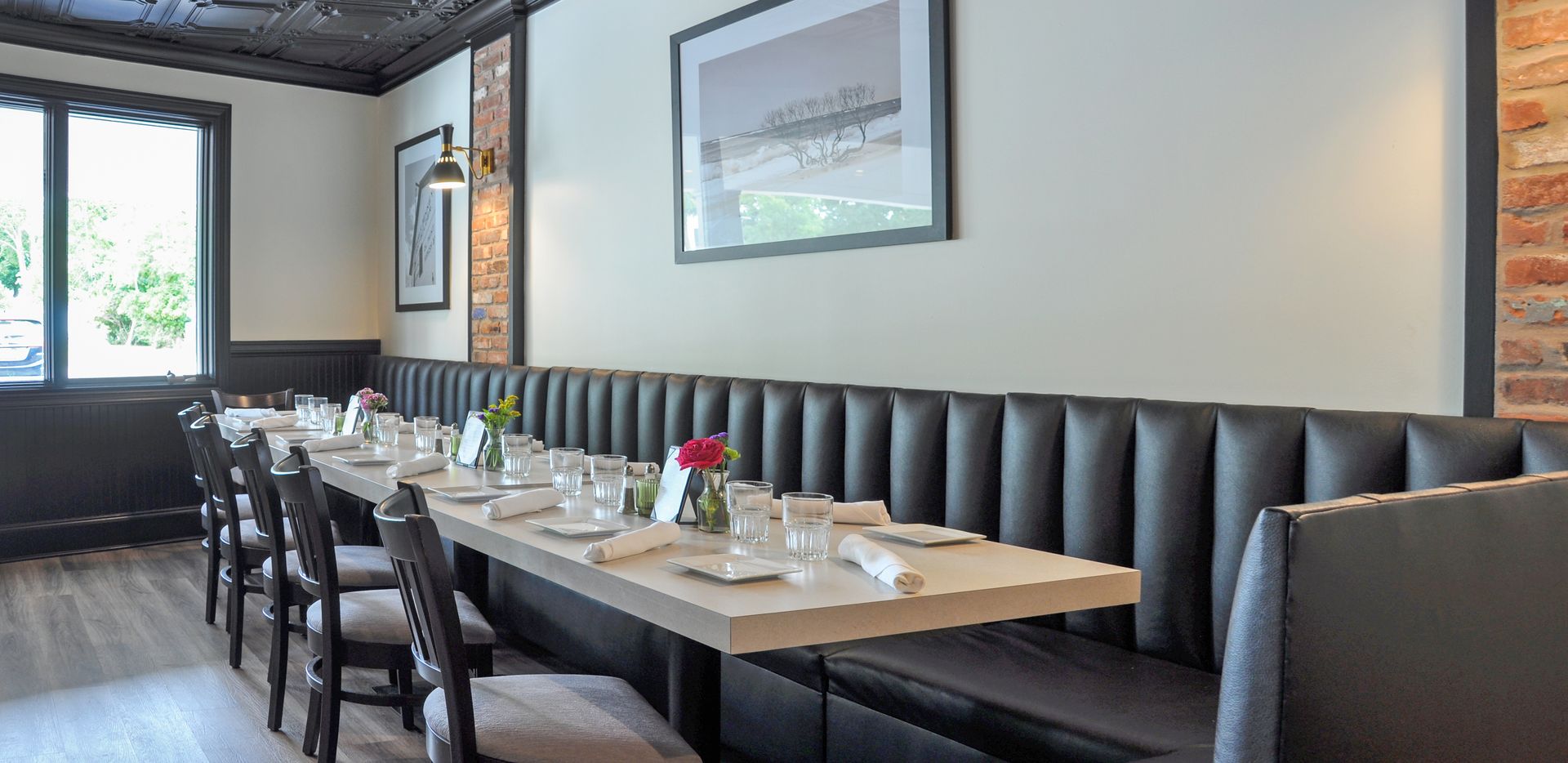 A long table and chairs in a restaurant with a picture on the wall.