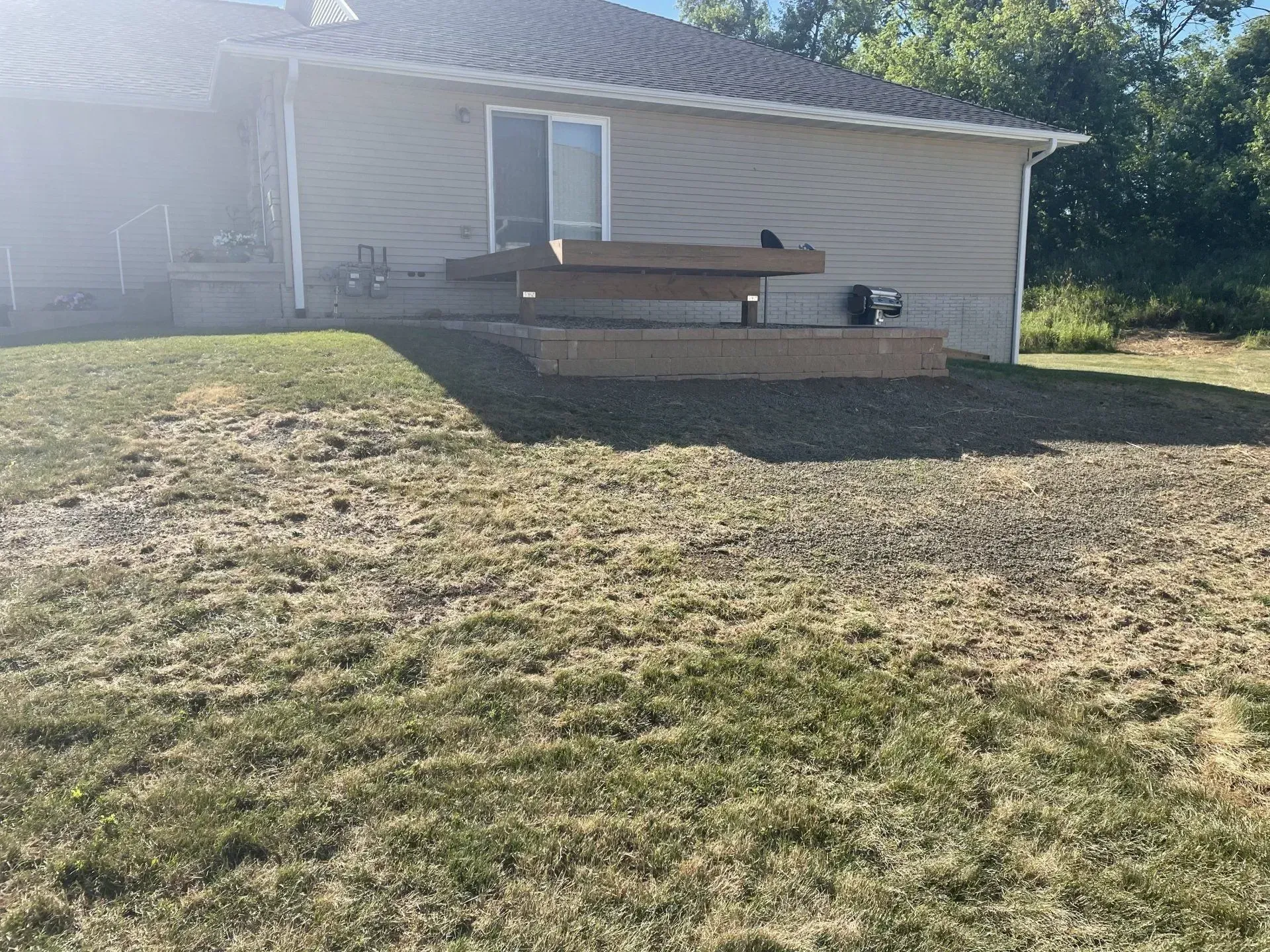 Backyard with a raised wooden deck attached to a light-colored house. Dry grass covers the foreground.