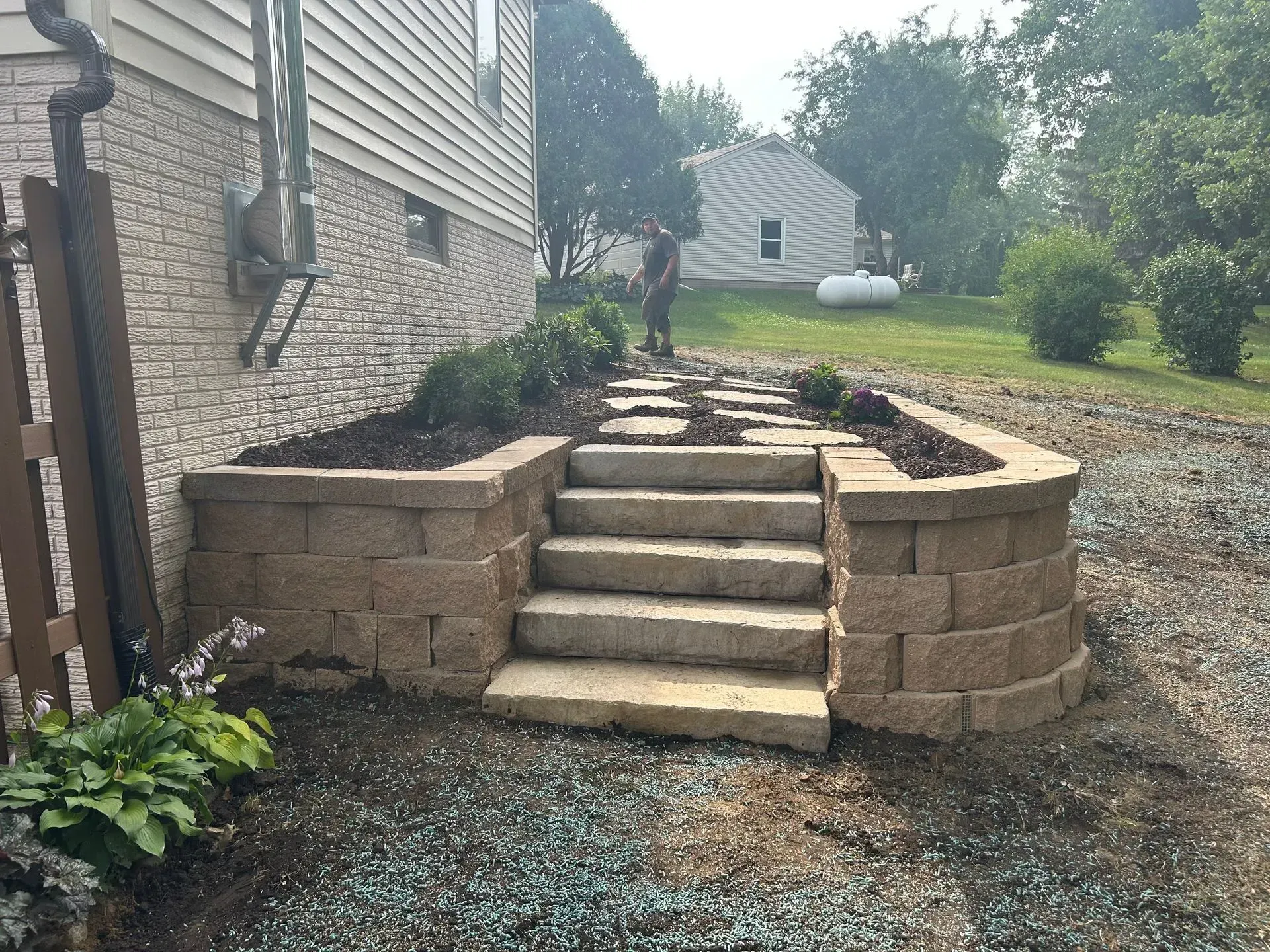 Stone steps leading up to a landscaped area with a building on the left and a yard in the background.