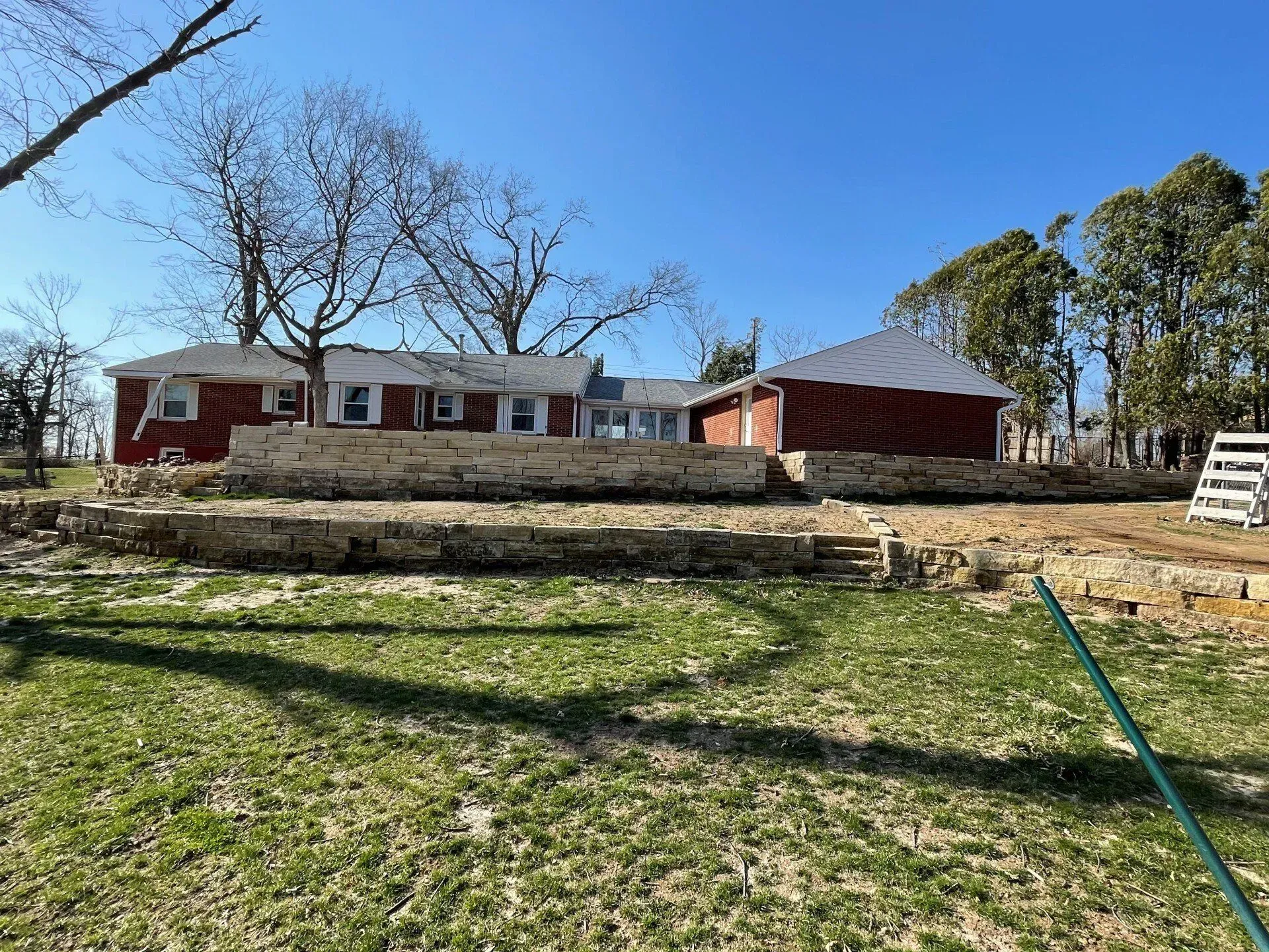 Red brick house with stone retaining walls, grassy yard, and blue sky.