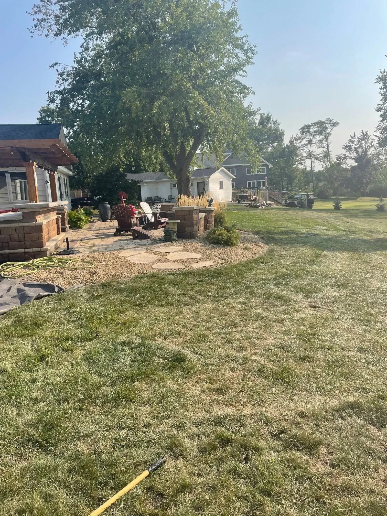 Backyard with a brick patio, fire pit, and a large tree, on a sunny day.