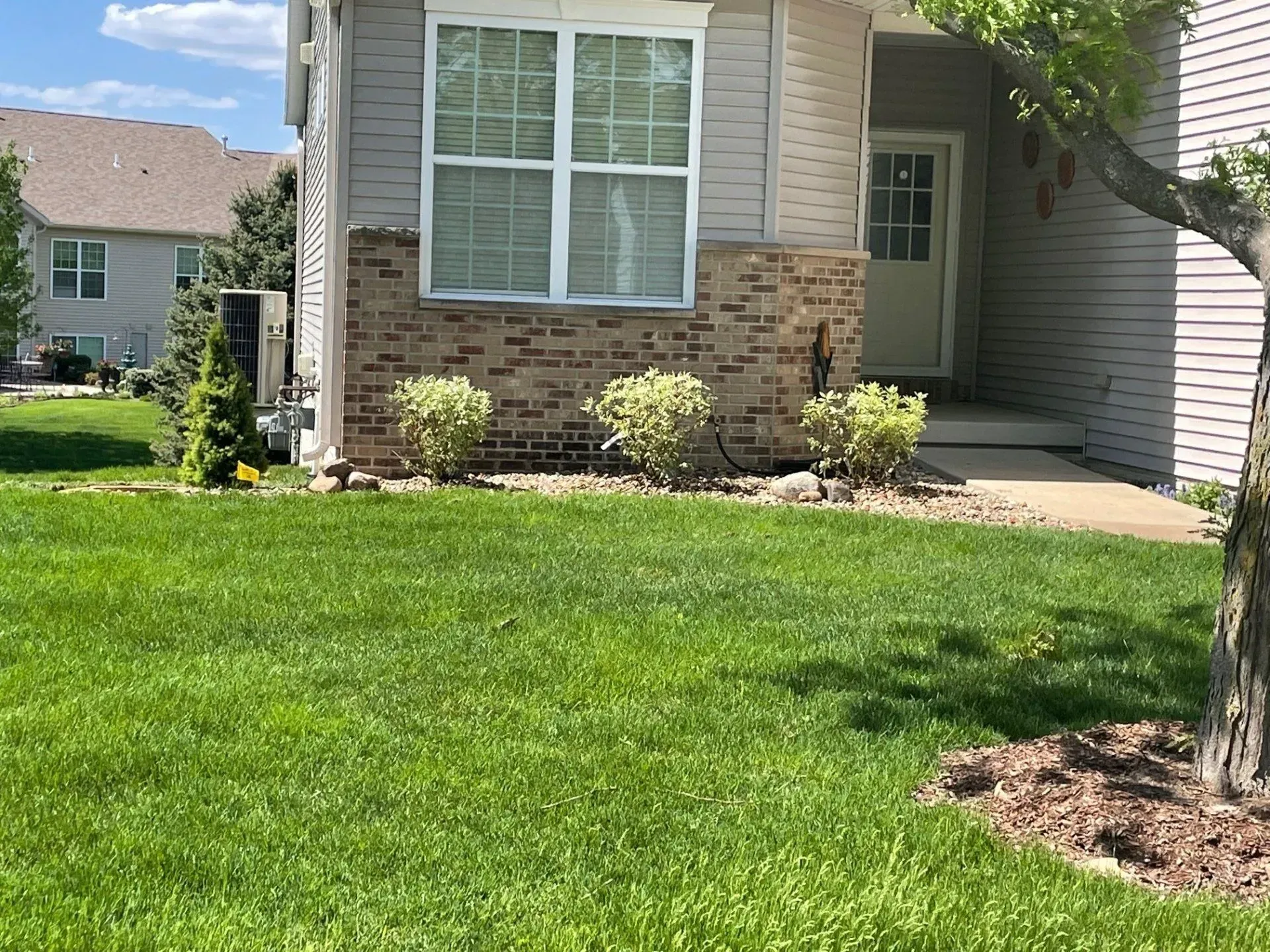 Exterior of a light-colored townhouse with green lawn and small shrubs. Brick accents on the facade.