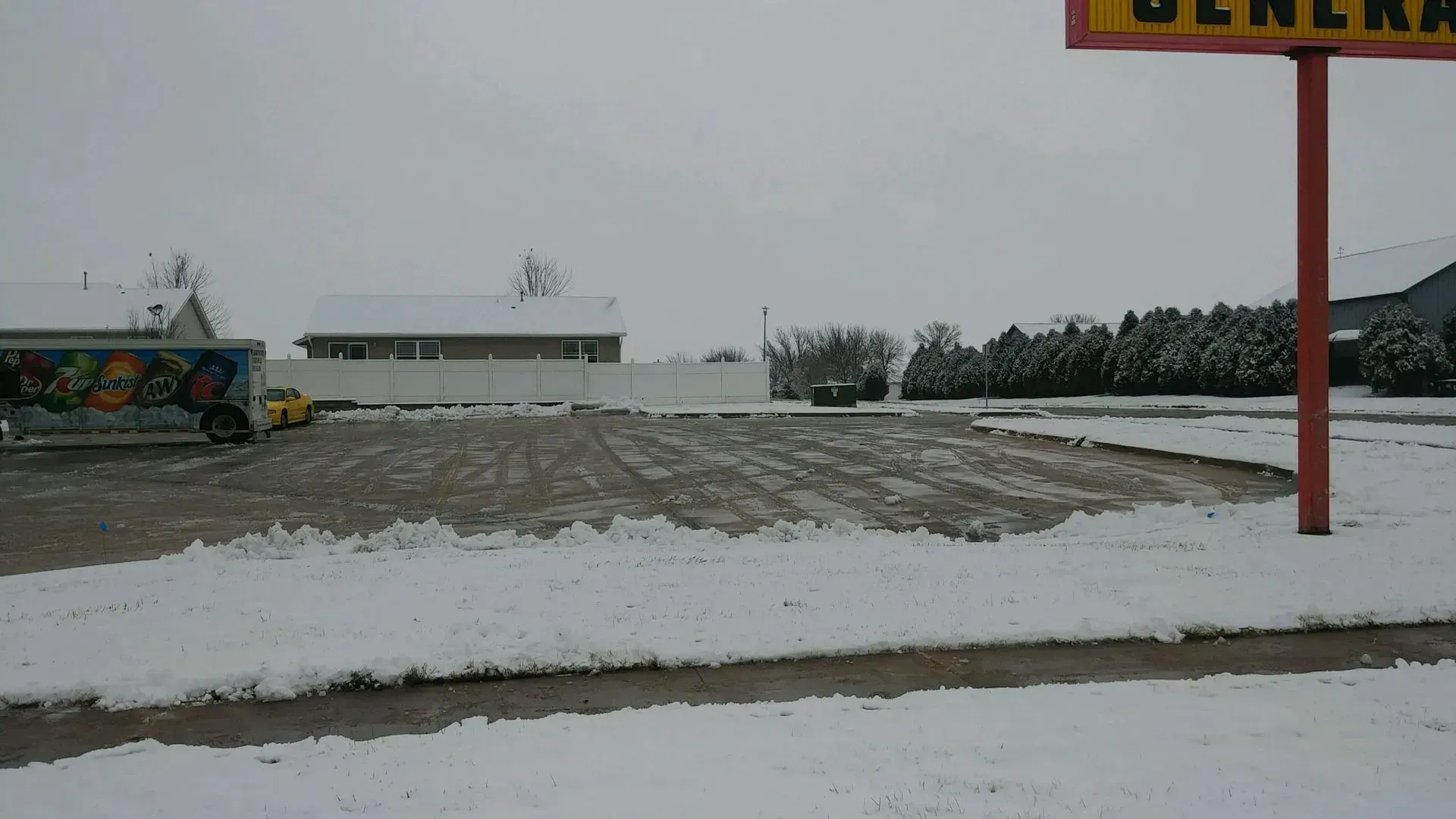 Snow-covered parking lot with a General Dollar store sign in the right corner, a truck on the left, overcast skies.