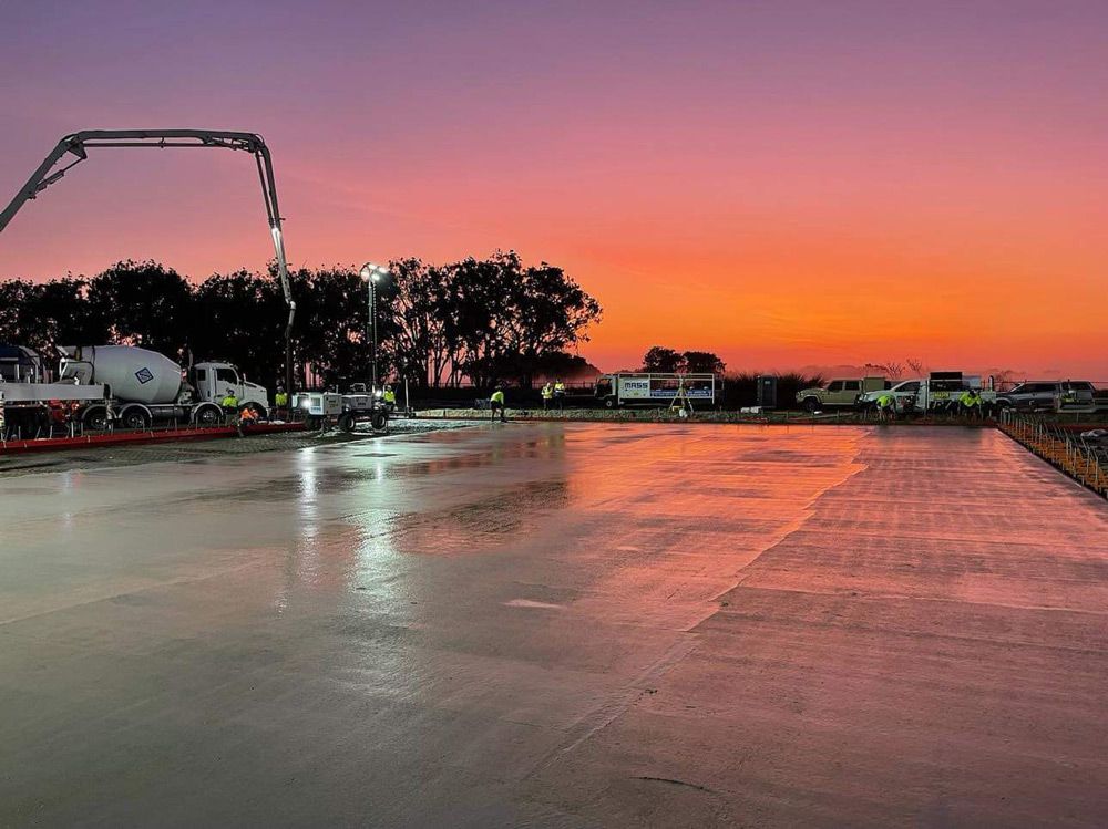A Concrete Pump Is Pouring Concrete Into a Parking Lot at Sunset — Mass Construction Group Australia Pty Ltd in South Mackay, QLD