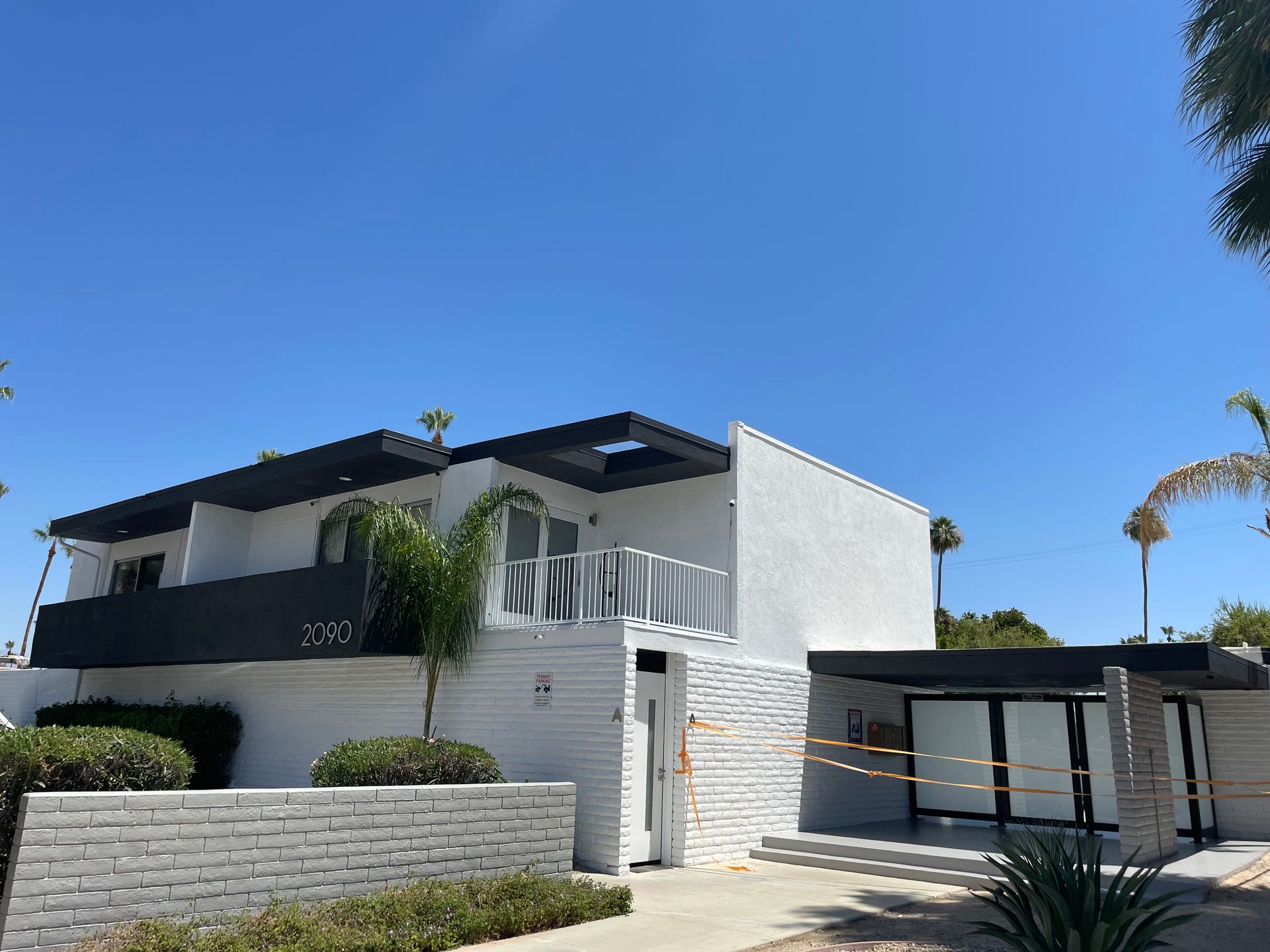 Modern white building with black trim against a blue sky, palm trees nearby.