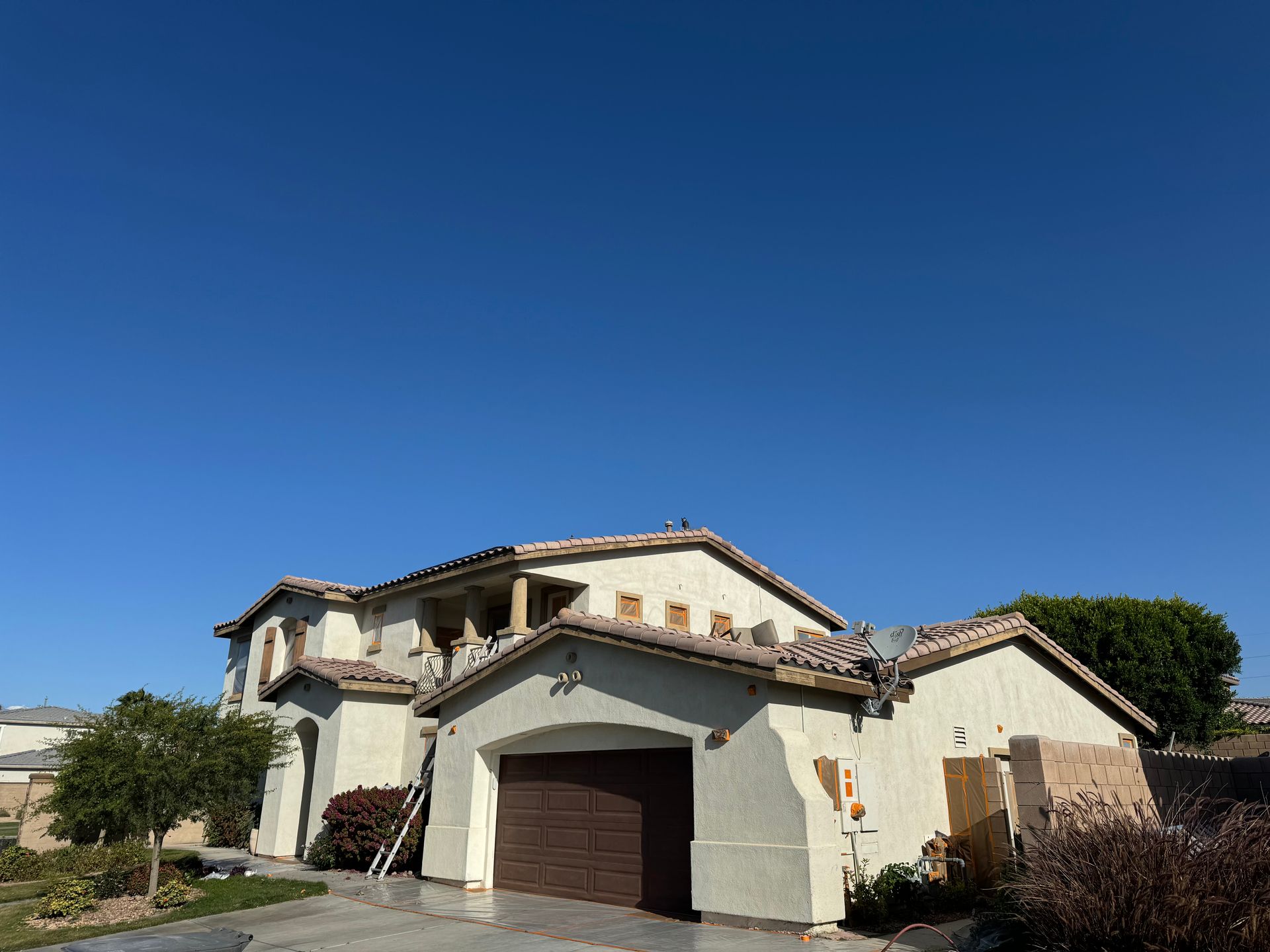 Two-story beige house with a brown garage door under a bright blue sky.