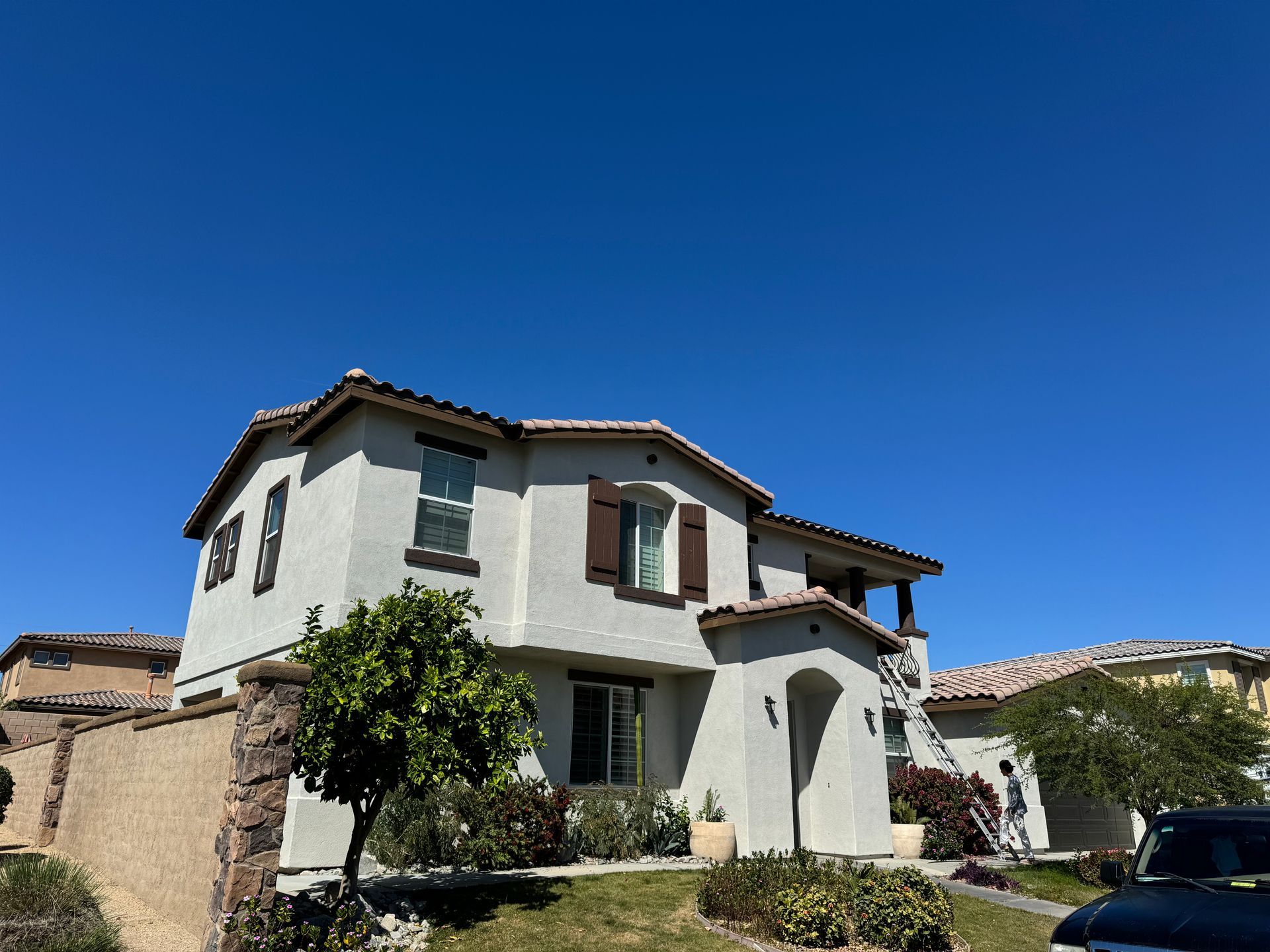 Two-story stucco house with brown shutters and trim against a clear blue sky.