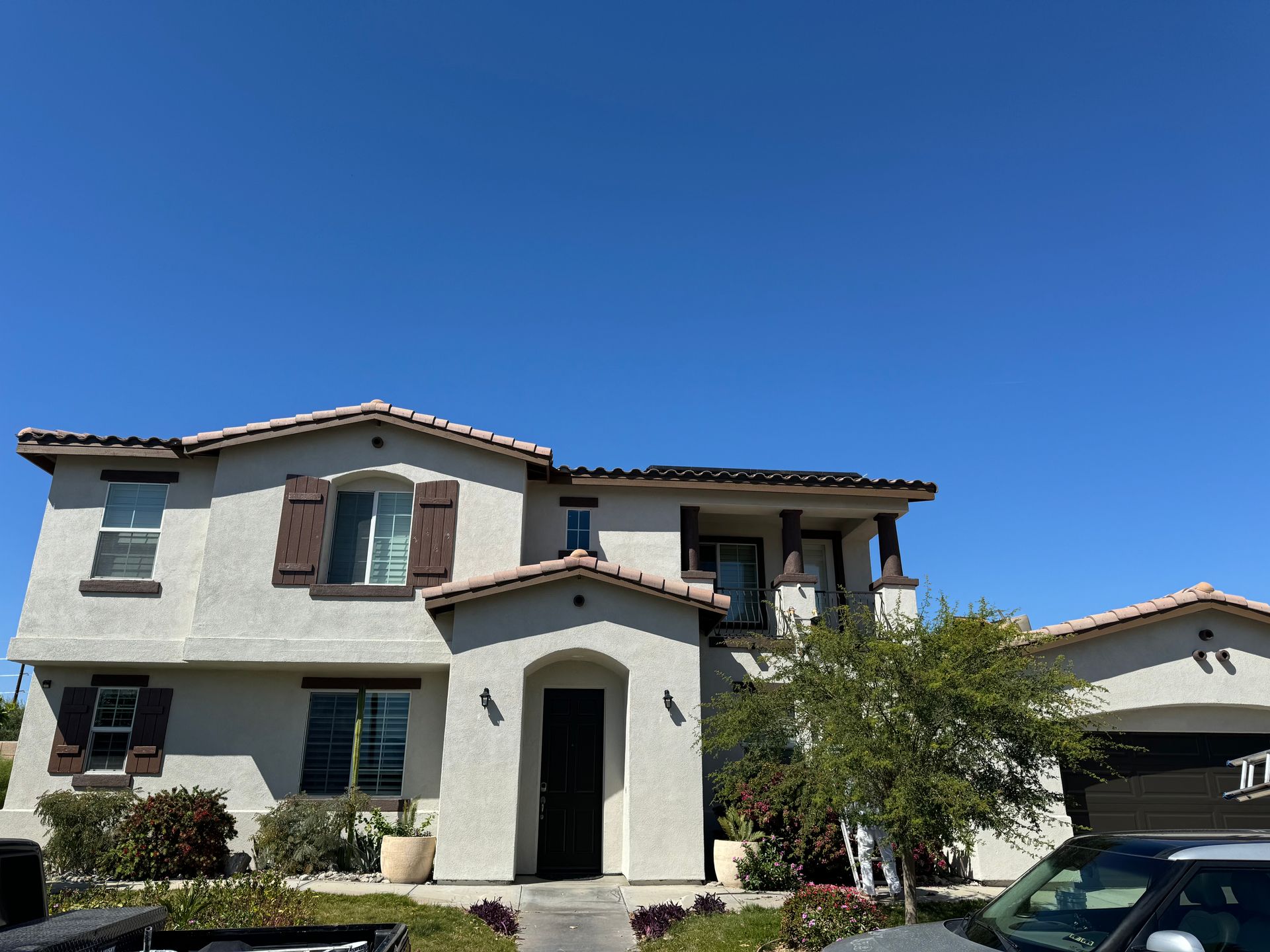 Two-story stucco house with brown shutters and a dark front door against a clear blue sky.
