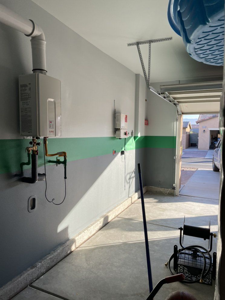 Garage interior with a water heater, exhaust pipe, and plumbing. Green and gray walls, concrete floor, garage door open.