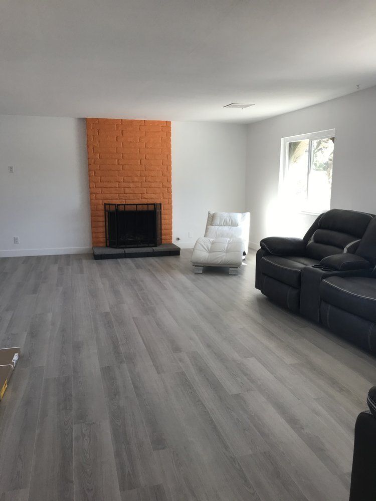 A living room with gray flooring, orange brick fireplace, white walls, and black leather sofa.