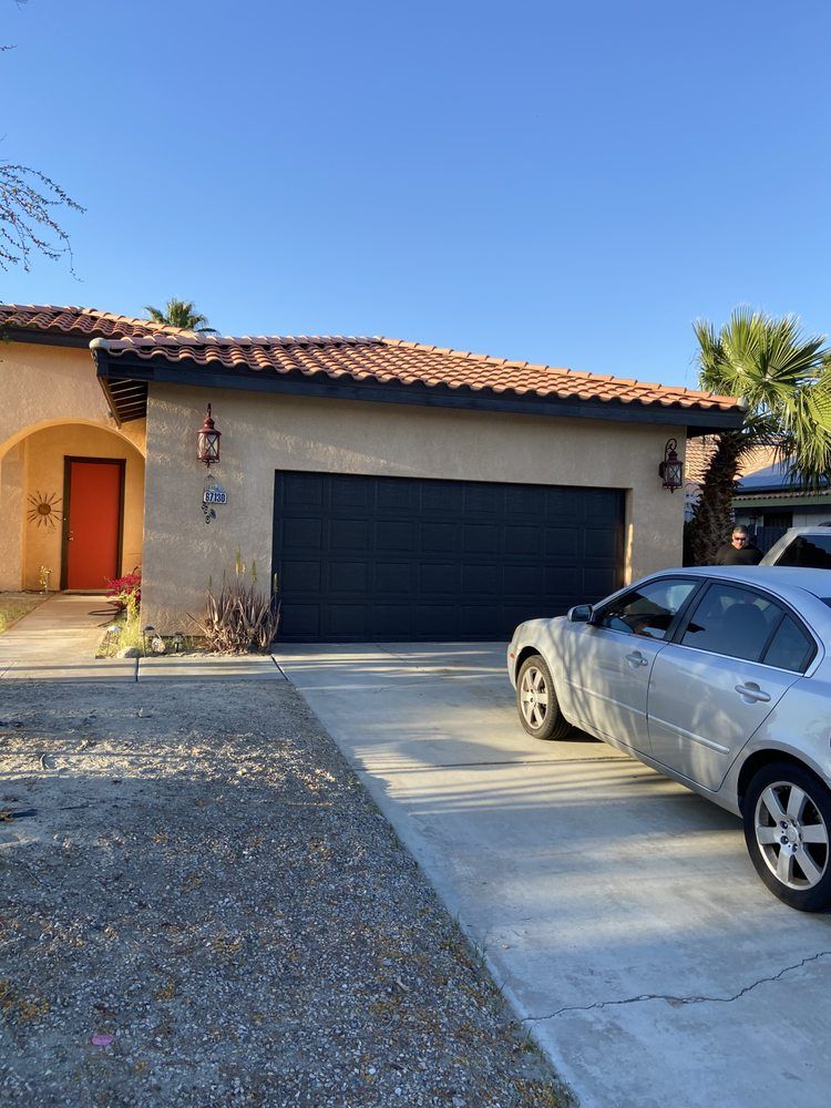 Tan house with orange door, black garage door, silver car, and blue sky.