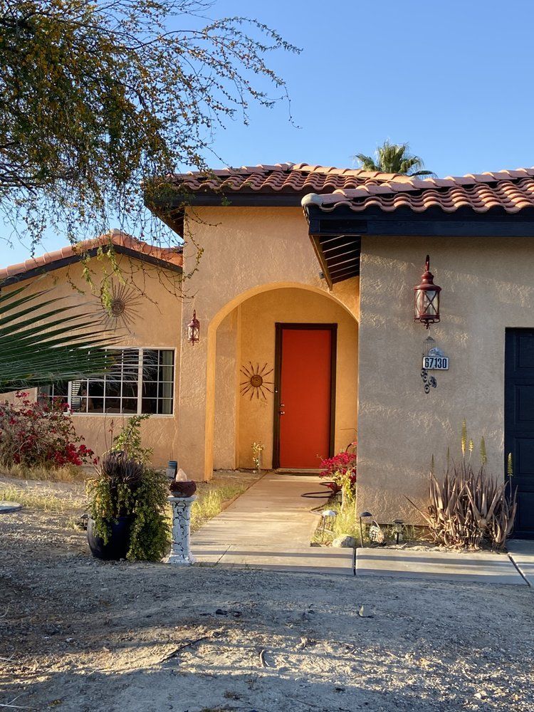 Tan stucco house with orange door, red tile roof, and arched entryway.