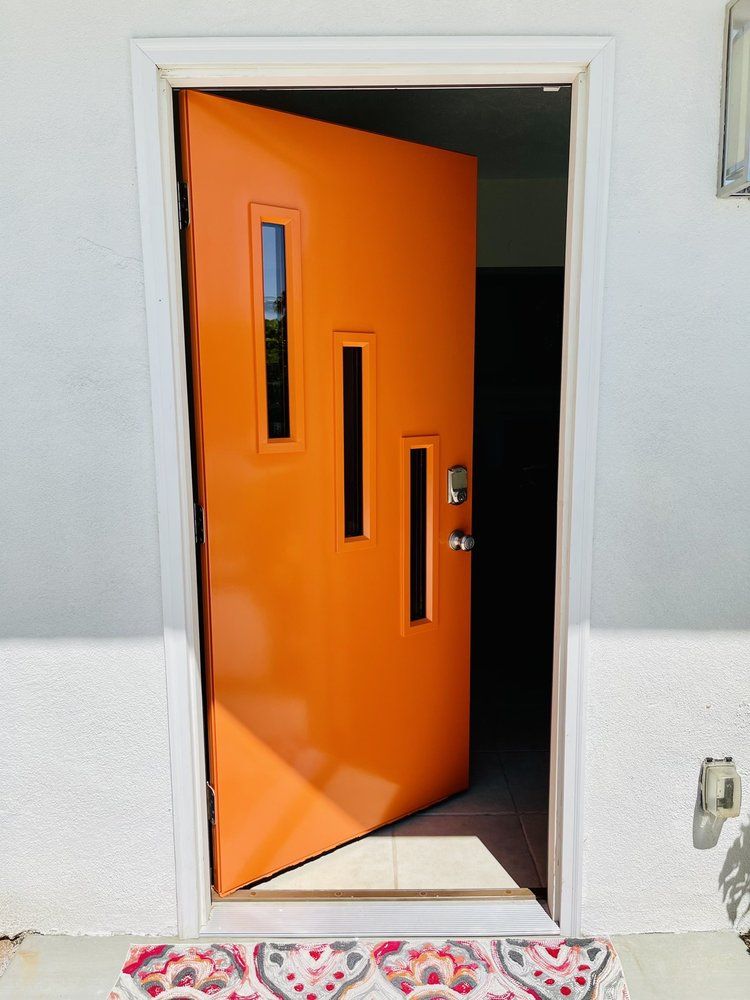 Orange front door with rectangular windows, slightly ajar, set in a white door frame.