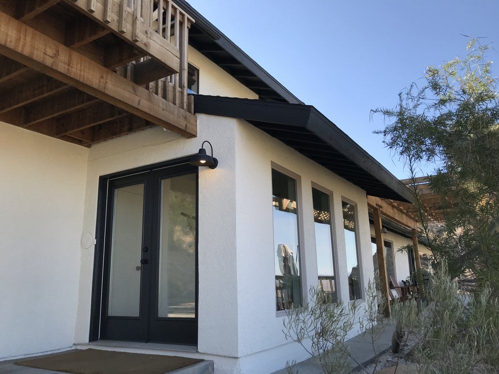White stucco house with black trim and door, a wooden deck, and large windows.