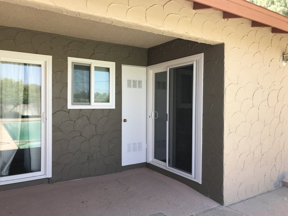 Exterior view of a building with a sliding glass door and windows. Dark brown textured stucco on walls.