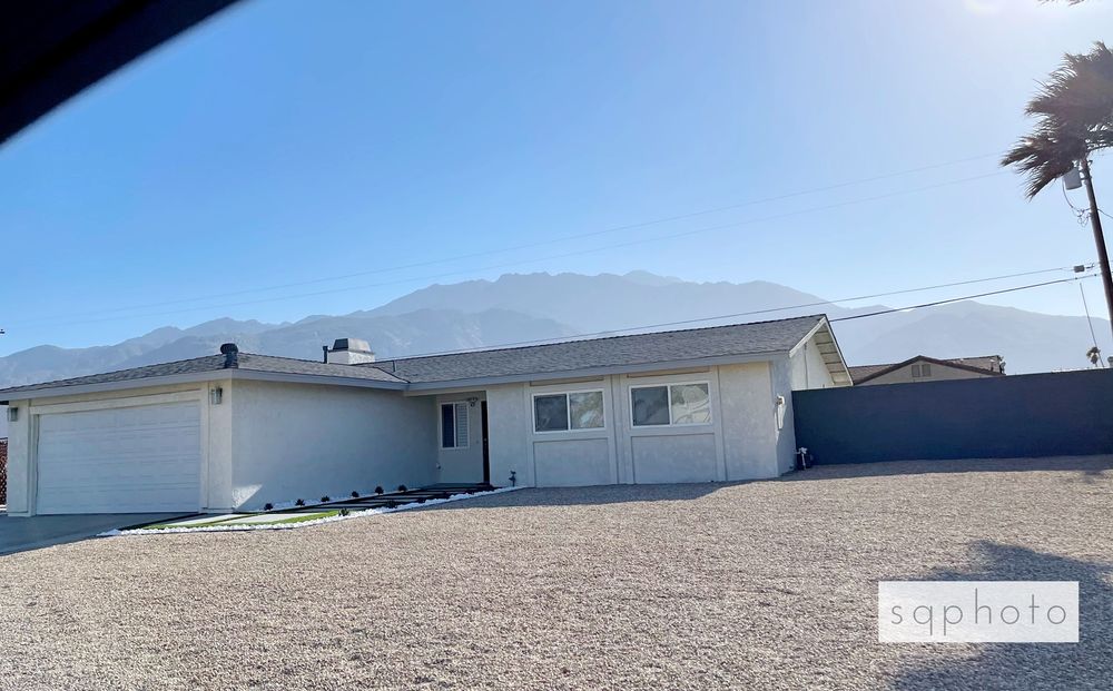 White house with grey roof and garage against a backdrop of mountains and a blue sky.