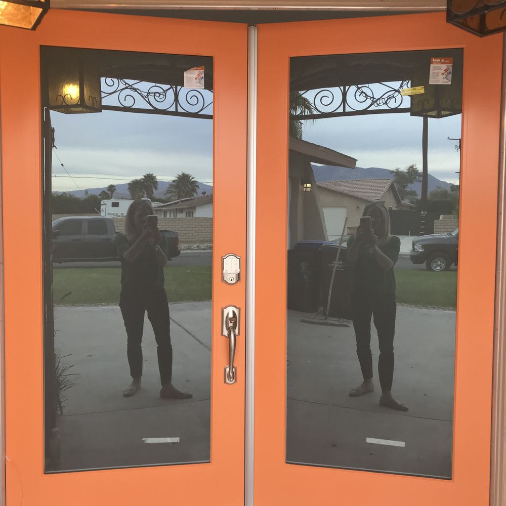 Orange double doors reflecting a person taking a photo; outside, houses and a car are visible.