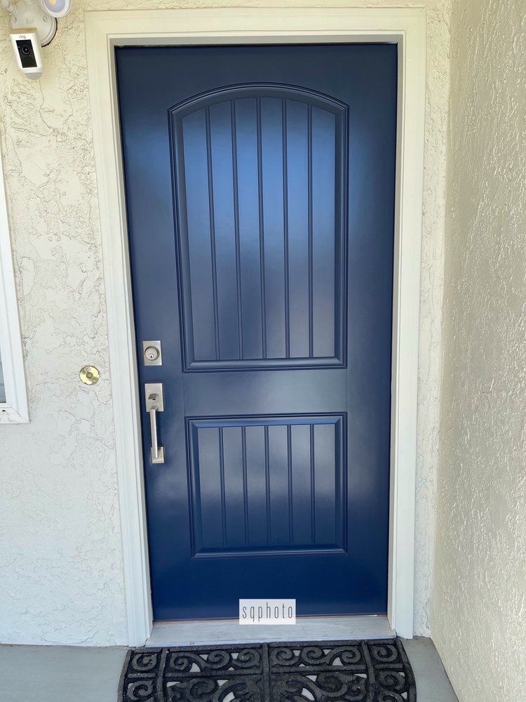 Blue front door with vertical panels, silver hardware, and a welcome mat.