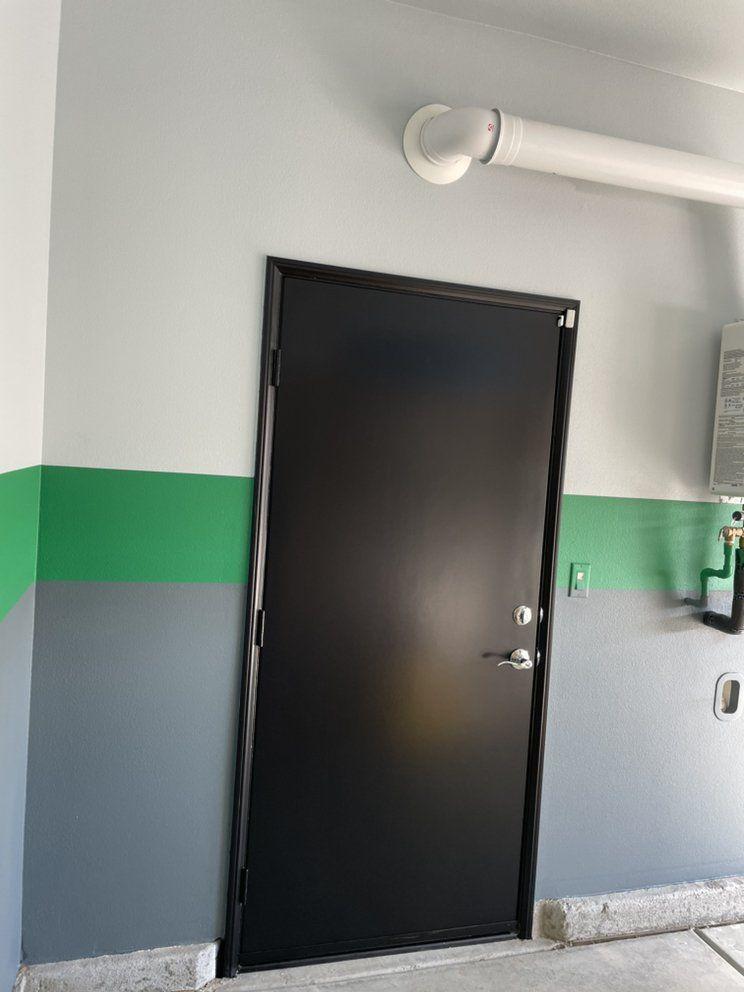 Black door in a garage with green and gray painted walls, and a white pipe above.