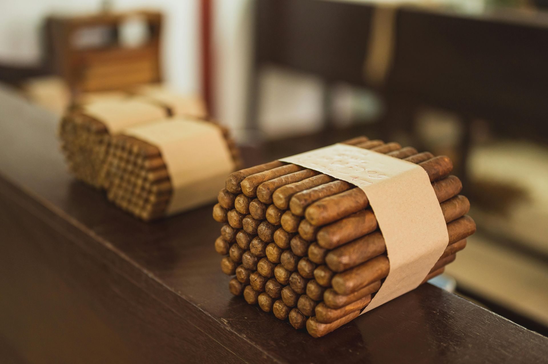 Bundles of brown rolled cigars tied with tan bands on a table, with a blurred stack in the background