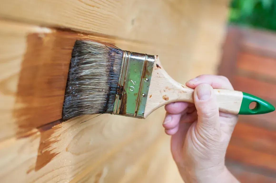 A person is painting a wooden wall with a brush.