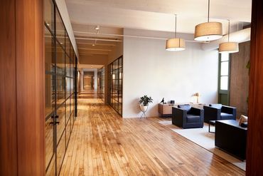 A hallway in an office building with wooden floors and chairs.