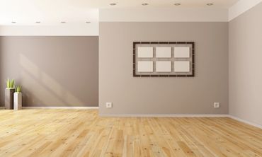 An empty room with a wooden floor and a picture frame on the wall.