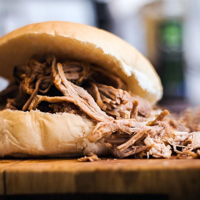 A pulled pork sandwich is sitting on a wooden cutting board.
