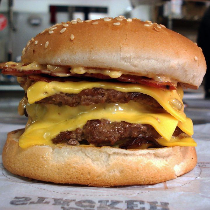 A hamburger with cheese and bacon sits on a piece of paper that says ' zycker ' on it