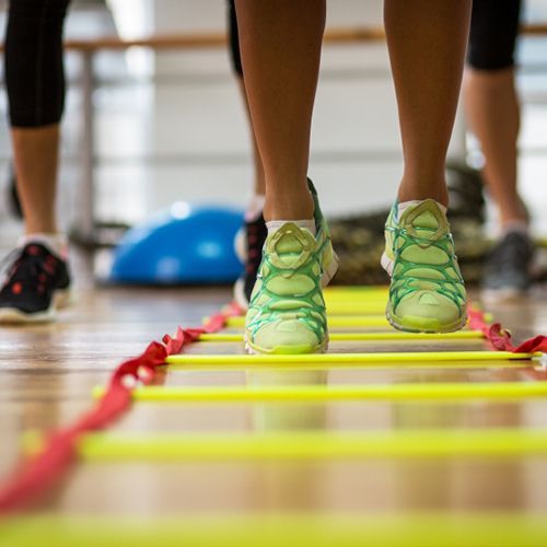 A person is standing on a yellow ladder in a gym.