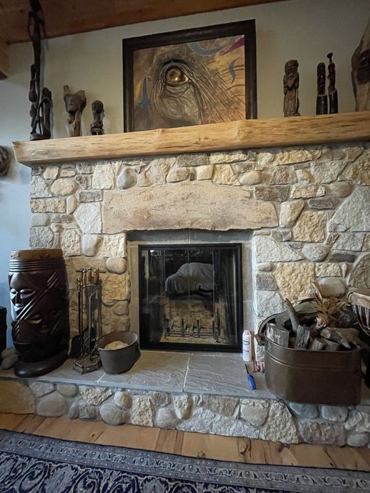 A living room with a stone fireplace and a painting on the mantle.