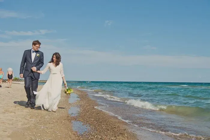 A bride and groom are walking on the beach.