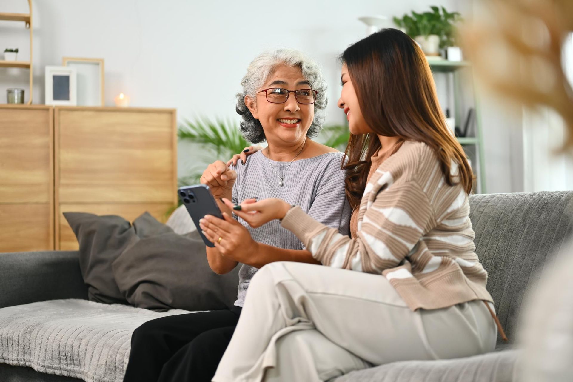 Woman showing phone to another woman, both smiling on a sofa.