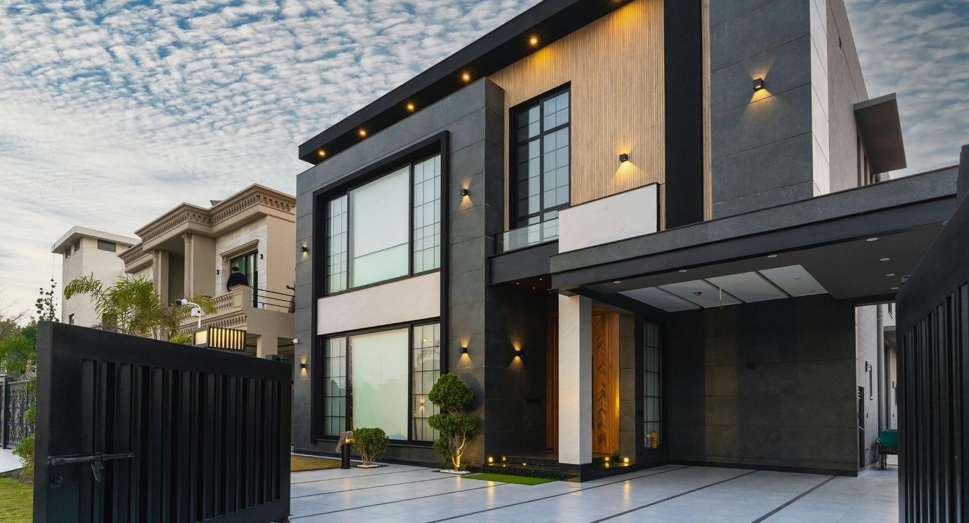 Modern two-story house with black and gray exterior, large windows, and a driveway at dusk