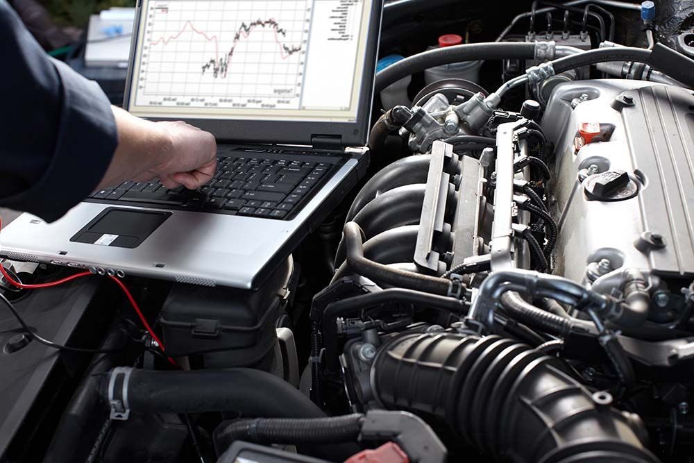 A man is working on a car engine with a laptop