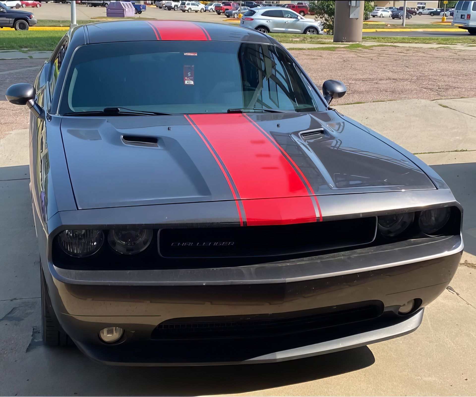 Black Dodge Challenger with red racing stripe parked outdoors, front view.