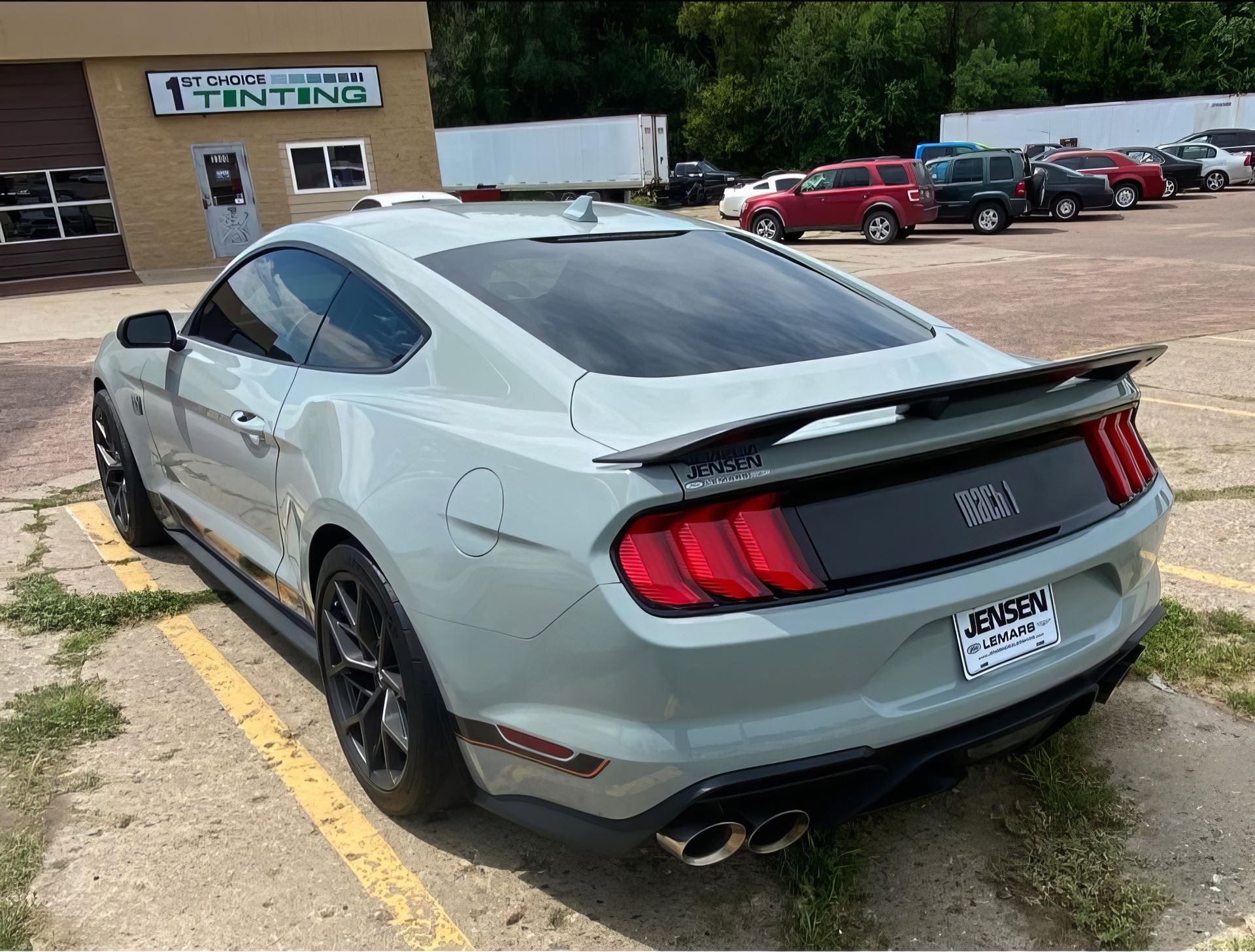 Gray sports coupe parked by a storefront, rear view with black spoiler and red taillights.