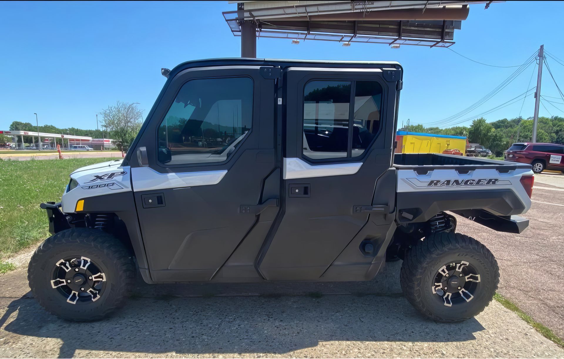 Black four-door utility vehicle parked on a gravel road in a sunny rural setting